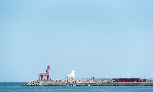 ihotewoo lighthouse in jeju island with a red horse statue and a white horse statue on a dock